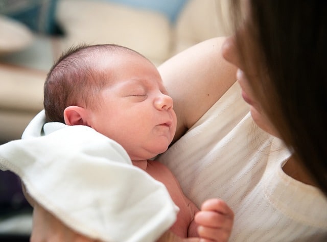 Jeune couple souriant avec un bébé dans les bras, entouré de vêtements et jouets pour enfants